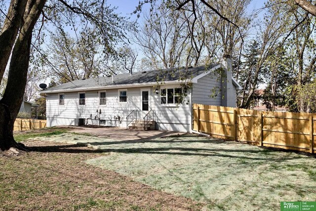 rear view of house with central air condition unit, entry steps, a lawn, and fence