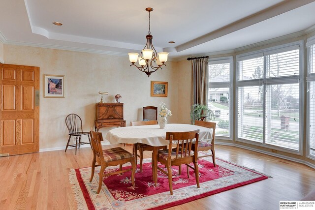 dining space with a chandelier, light wood-type flooring, and a tray ceiling