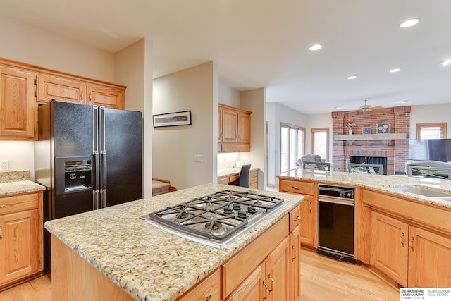 kitchen with black fridge with ice dispenser, stainless steel gas stovetop, open floor plan, a kitchen island, and light wood-style flooring