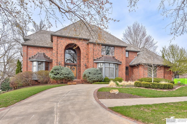 traditional-style house with a high end roof, brick siding, and a front yard