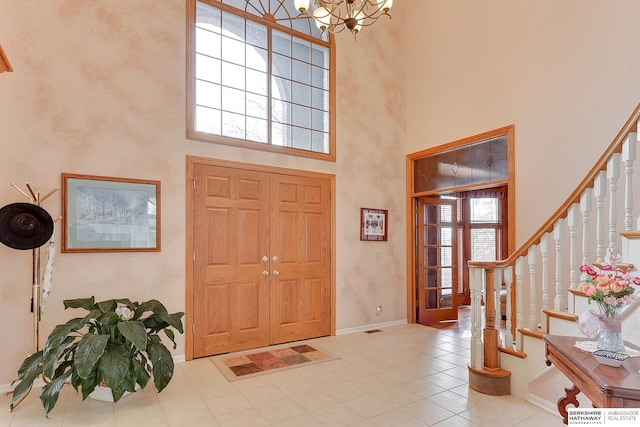 tiled foyer featuring stairs, a towering ceiling, baseboards, a notable chandelier, and visible vents