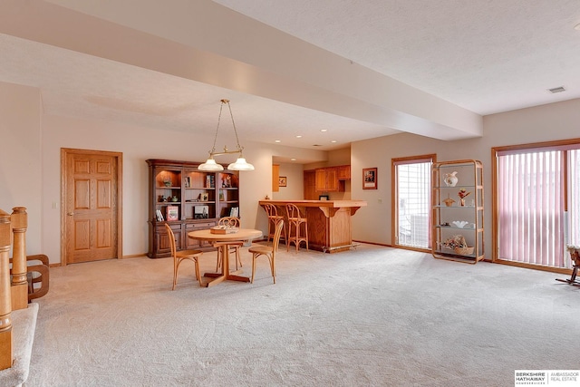 dining space featuring light colored carpet, a bar, and baseboards