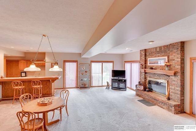 dining room with light colored carpet, a brick fireplace, and a textured ceiling