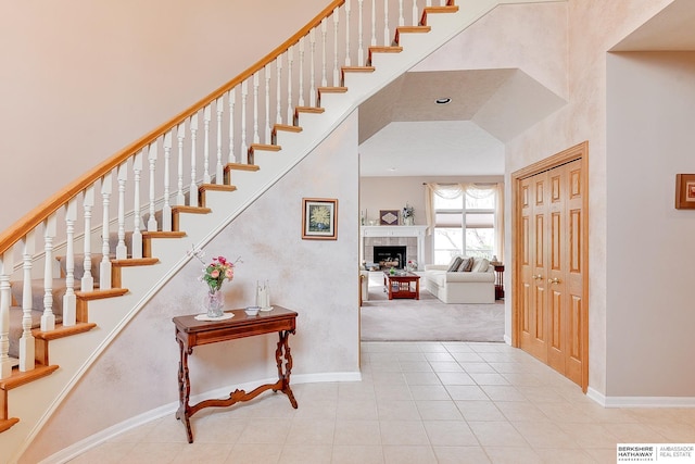 stairway with tile patterned flooring, baseboards, a fireplace, carpet floors, and a towering ceiling
