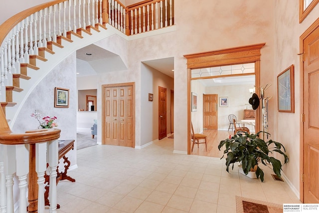 entryway with a high ceiling, light tile patterned flooring, baseboards, stairs, and arched walkways