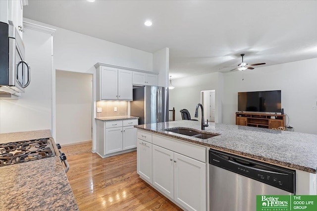 kitchen with light wood finished floors, stainless steel appliances, a sink, white cabinetry, and ceiling fan