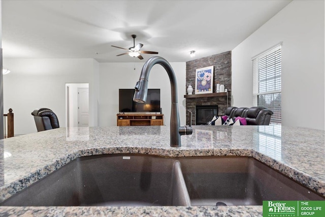 details featuring a stone fireplace, ceiling fan, light stone counters, and a sink