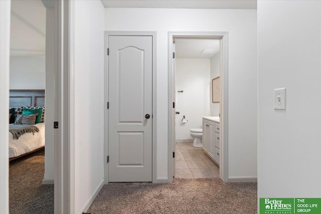 corridor featuring light carpet, light tile patterned flooring, and baseboards