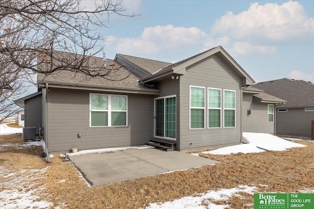 snow covered back of property with a patio area, a shingled roof, and central AC unit