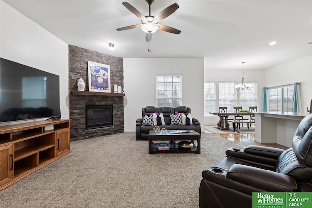 living area with a stone fireplace, carpet flooring, and ceiling fan with notable chandelier