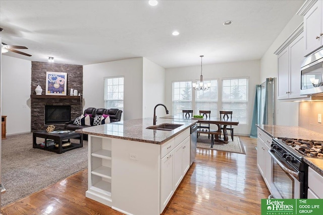 kitchen with dark stone counters, a sink, light wood-type flooring, stainless steel appliances, and a center island with sink