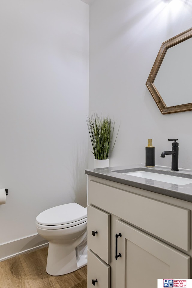 bathroom featuring baseboards, wood finished floors, toilet, and vanity