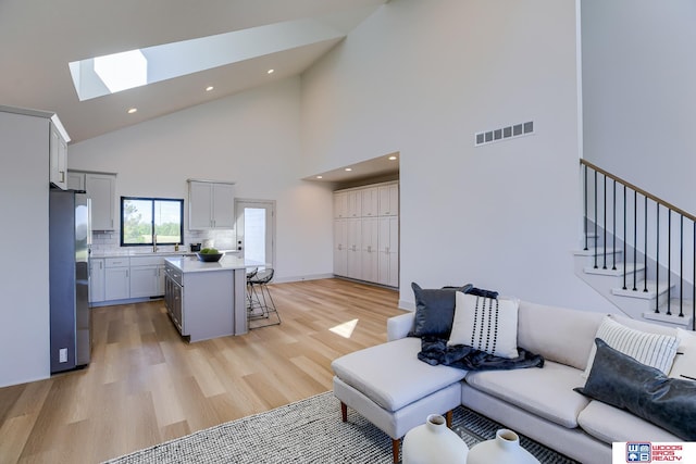 living area with high vaulted ceiling, a skylight, light wood finished floors, visible vents, and recessed lighting