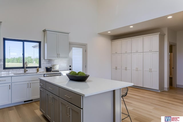 kitchen featuring gray cabinets, a towering ceiling, a sink, and light wood finished floors