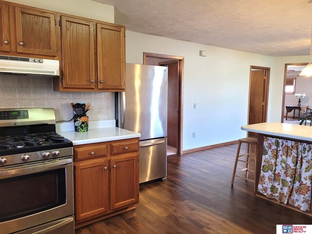 1321 Frances St, Goehner, NE 68364 - kitchen with under cabinet range hood, stainless steel appliances, light countertops, dark wood-type flooring, and brown cabinetry