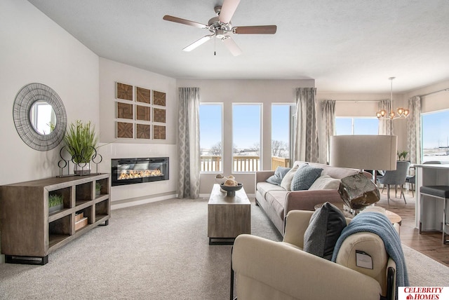 living area featuring a glass covered fireplace and ceiling fan with notable chandelier