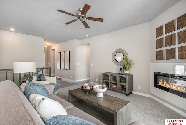 living area with a glass covered fireplace, baseboards, carpet flooring, and ceiling fan