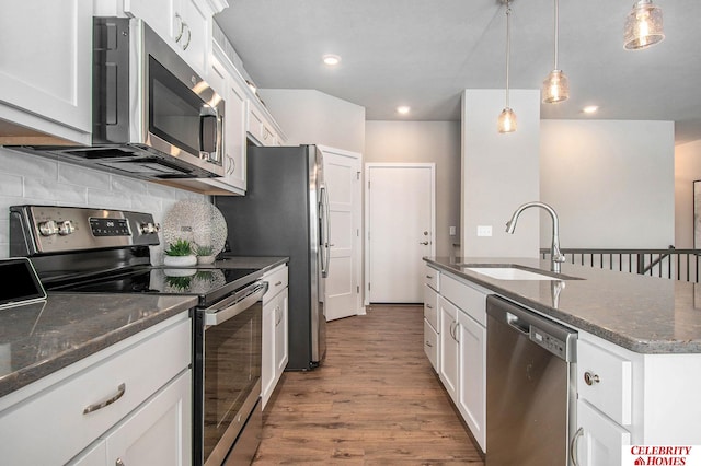 kitchen featuring an island with sink, stainless steel appliances, wood finished floors, a sink, and decorative backsplash