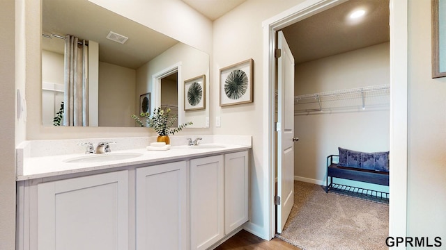 bathroom with a walk in closet, double vanity, visible vents, and a sink