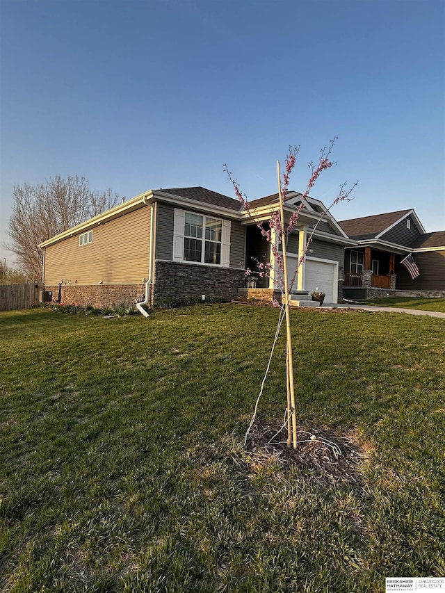 view of front of house with an attached garage, fence, stone siding, and a front yard