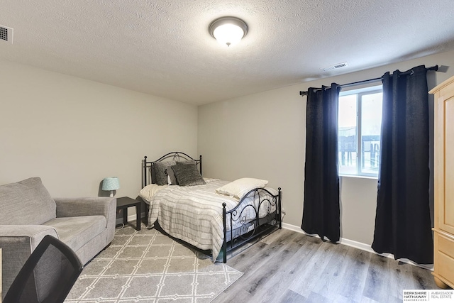 bedroom with light wood-style floors, visible vents, and a textured ceiling