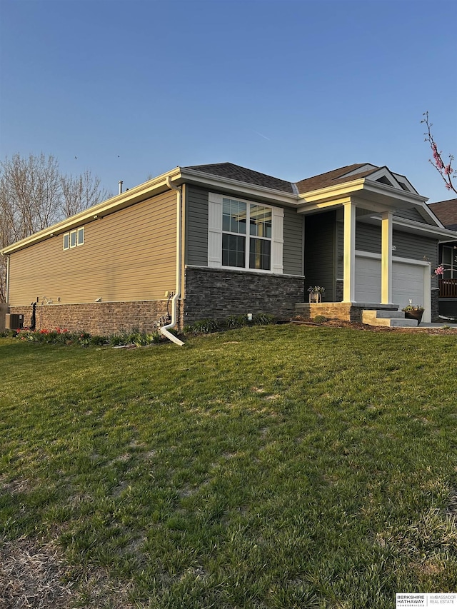 view of front of property featuring an attached garage, a front lawn, stone siding, and central AC