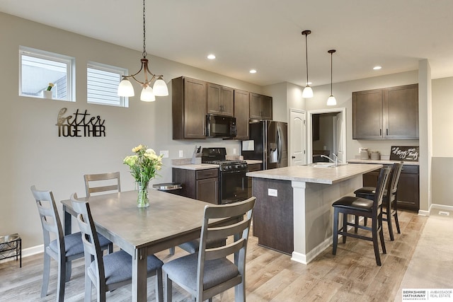 kitchen with light countertops, a breakfast bar, dark brown cabinetry, a kitchen island with sink, and black appliances