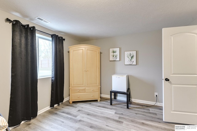 living area with baseboards, visible vents, a textured ceiling, and light wood-style floors