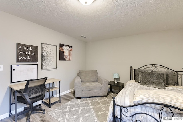 bedroom featuring baseboards, wood finished floors, visible vents, and a textured ceiling