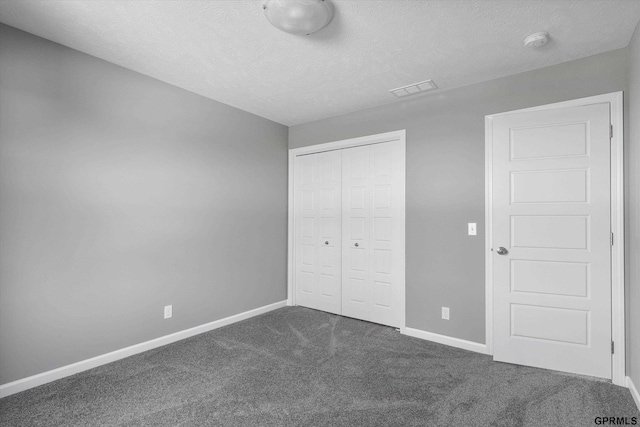 unfurnished bedroom with a textured ceiling, a closet, baseboards, dark colored carpet, and visible vents