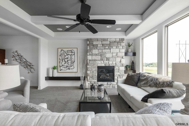 living room with a ceiling fan, a stone fireplace, carpet floors, and a raised ceiling