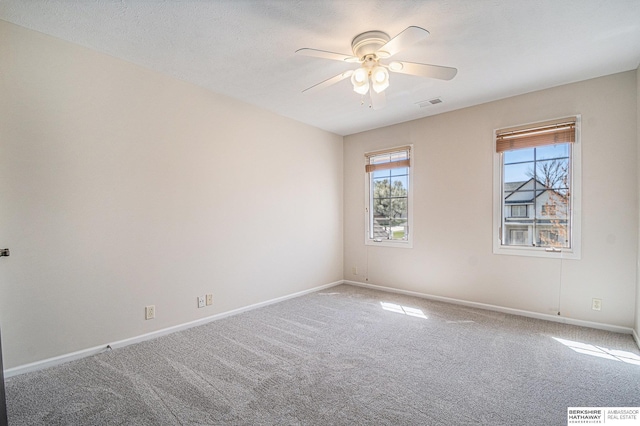 carpeted empty room with baseboards, a ceiling fan, and visible vents