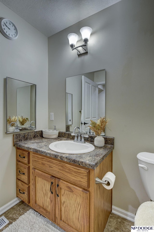half bathroom featuring a textured ceiling, vanity, baseboards, toilet, and visible vents