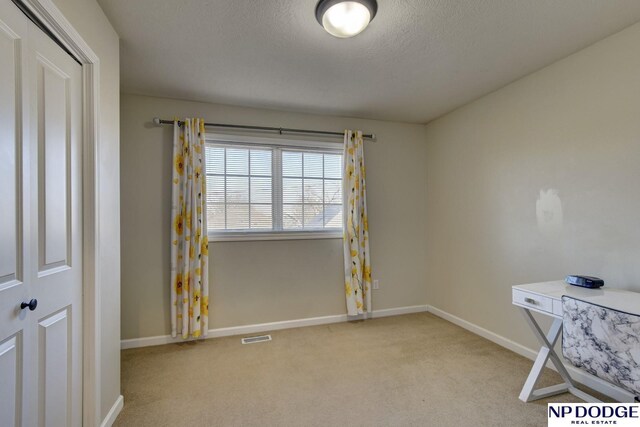 unfurnished office featuring baseboards, visible vents, a textured ceiling, and light colored carpet