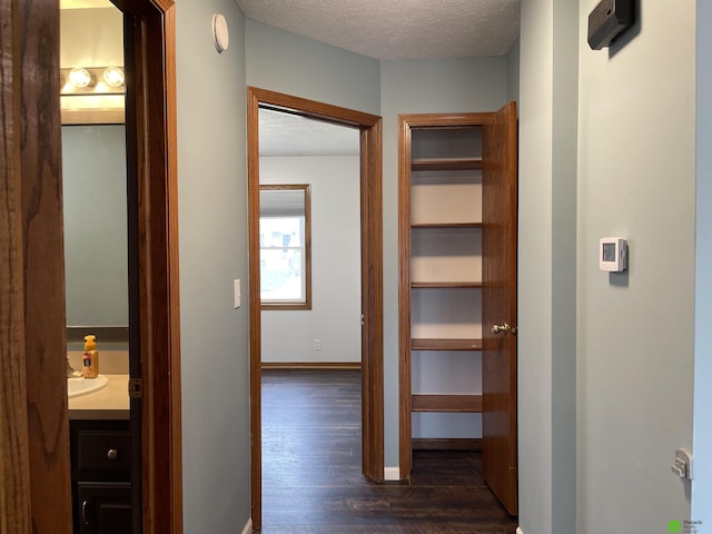 hall with dark wood-style flooring, baseboards, and a textured ceiling