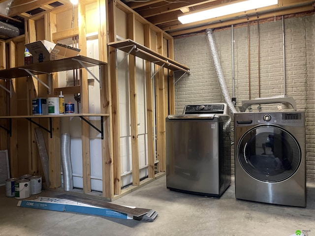 clothes washing area with brick wall, washing machine and clothes dryer, and laundry area