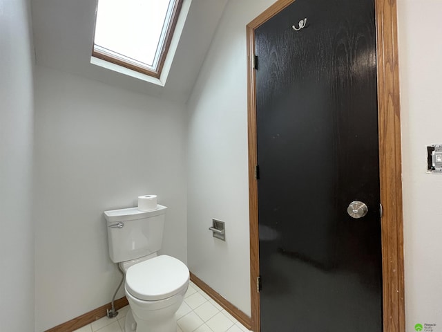 bathroom featuring tile patterned floors, baseboards, toilet, and vaulted ceiling with skylight