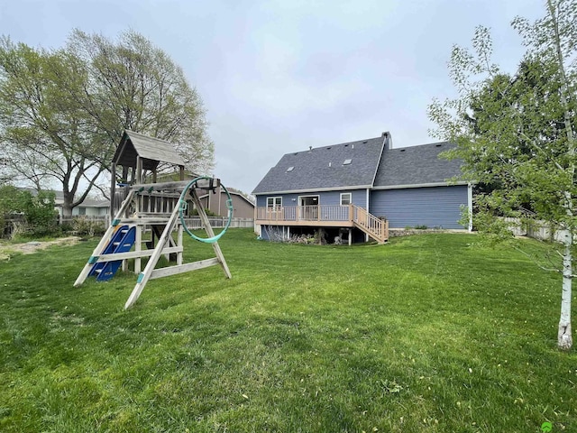 back of property with a playground, a deck, roof with shingles, fence, and a yard