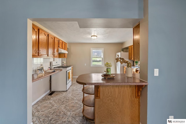 2725 Monroe St, Omaha, NE 68107 - kitchen featuring a kitchen breakfast bar, fridge, a peninsula, under cabinet range hood, and gas range gas stove