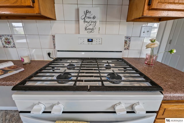 2725 Monroe St, Omaha, NE 68107 - room details featuring white gas range, dark countertops, decorative backsplash, and brown cabinets
