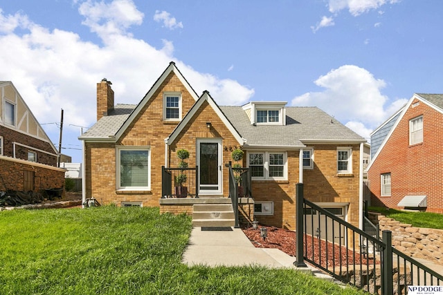 tudor-style house featuring a shingled roof, a chimney, a front lawn, and brick siding