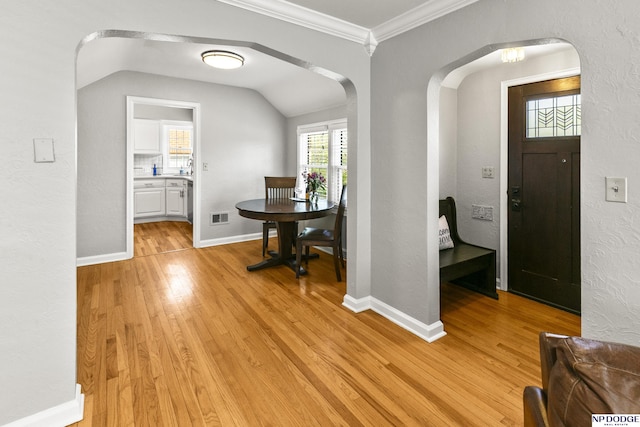 entryway featuring crown molding, visible vents, lofted ceiling, light wood-type flooring, and arched walkways