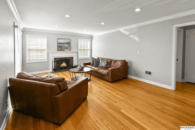 living area with crown molding, visible vents, a fireplace with flush hearth, and light wood-style floors