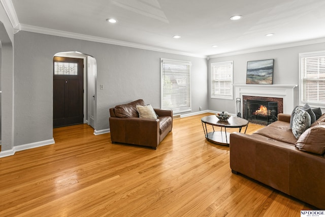 living area with crown molding, arched walkways, light wood-style flooring, and a premium fireplace