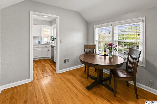 dining area featuring vaulted ceiling, plenty of natural light, light wood-style flooring, and visible vents