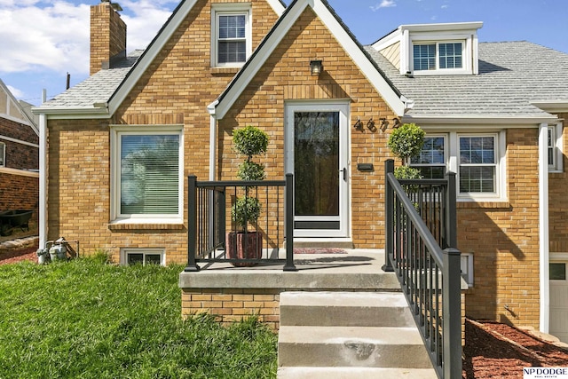bungalow featuring brick siding, a garage, roof with shingles, and a chimney