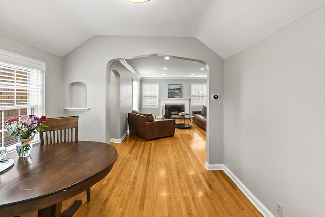 dining room with light wood-style floors, arched walkways, baseboards, and lofted ceiling