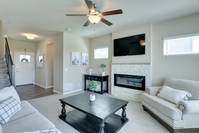 carpeted living area with visible vents, baseboards, a fireplace, stairs, and ceiling fan