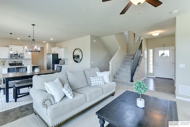 living room with stairway, ceiling fan with notable chandelier, dark wood-style flooring, visible vents, and recessed lighting