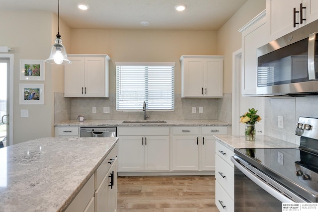 kitchen with a sink, light wood-style floors, stainless steel appliances, decorative light fixtures, and white cabinets
